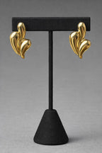 Gold earrings on a black stand against a gray background