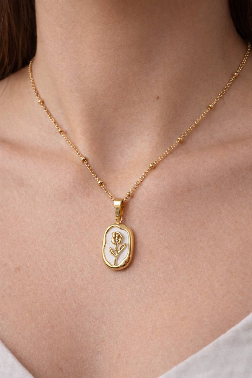 Gold necklace with a pendant featuring a white design on a person's neck.