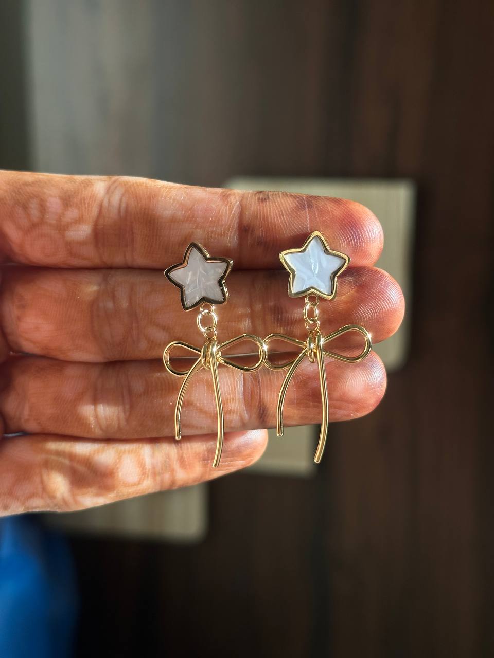 Star-shaped earrings with gold bows held in a hand against a neutral background