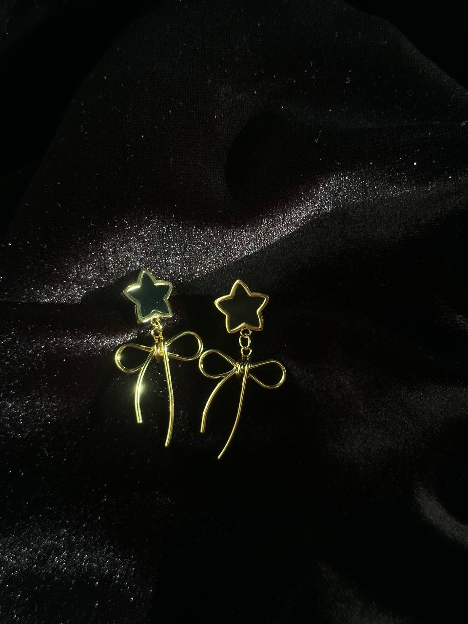 Gold star earrings with bows on a dark fabric background