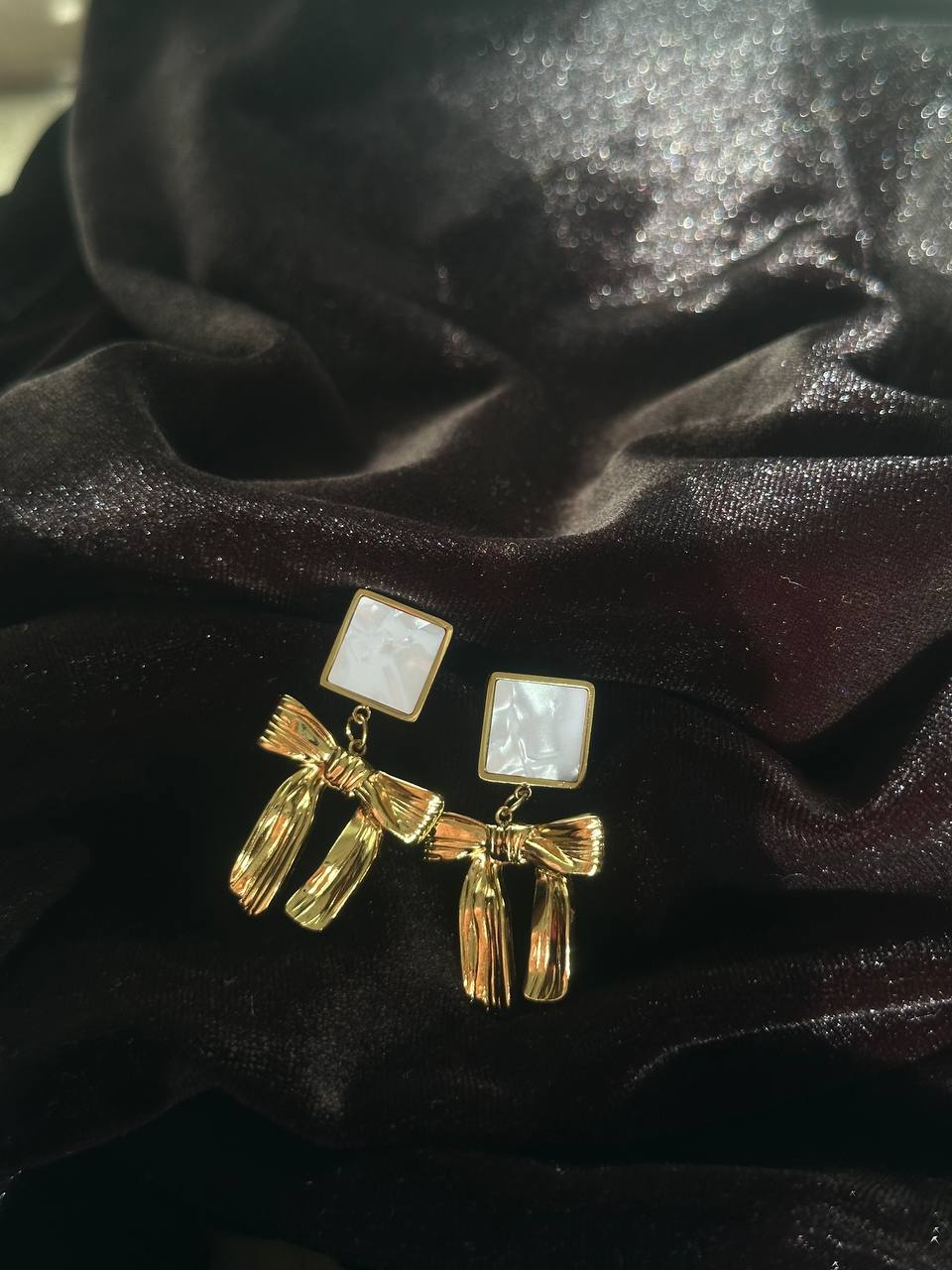 Gold earrings with bow design on a black fabric background