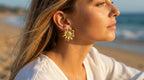 Woman wearing gold flower earrings on a beach