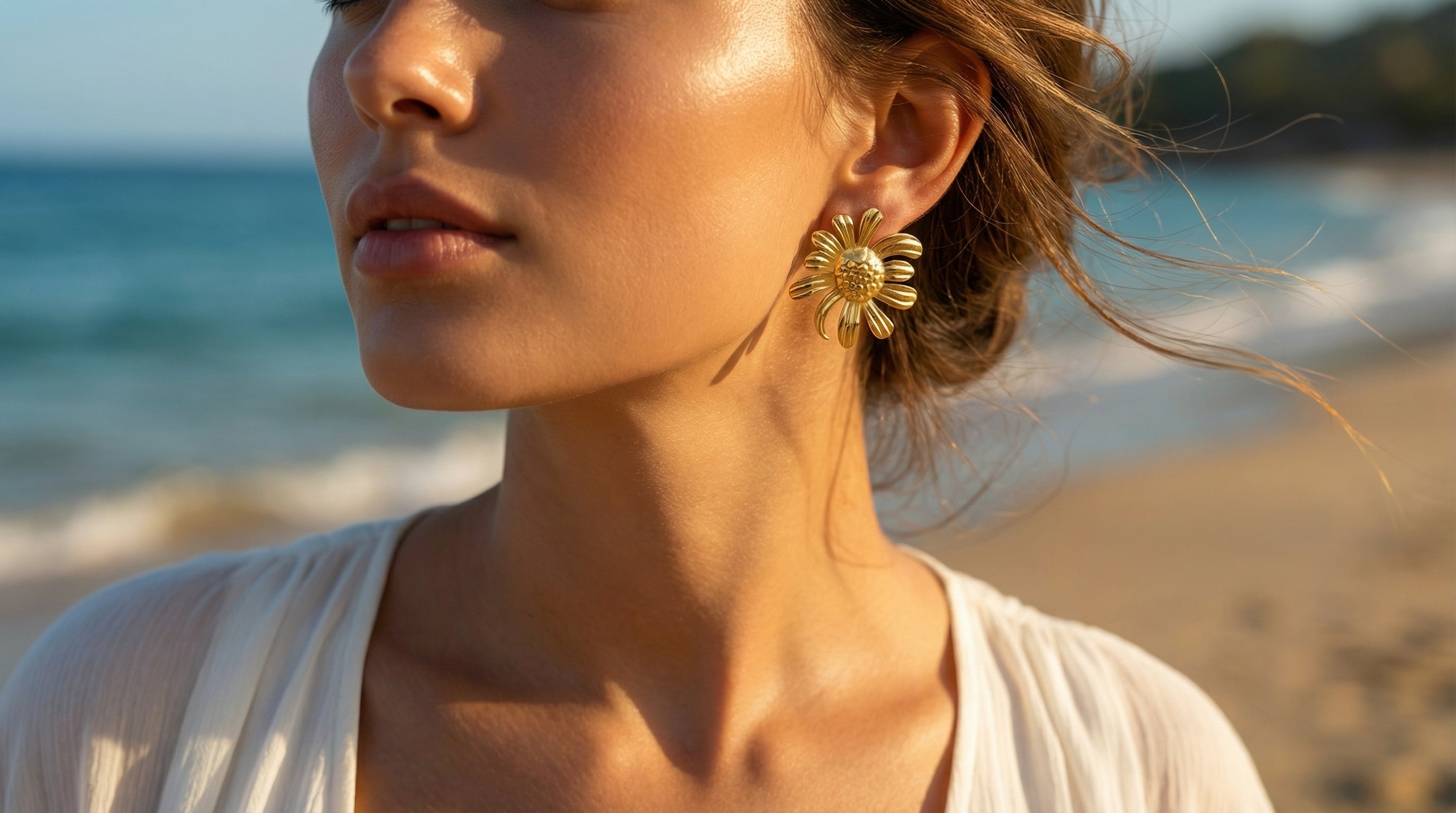 Woman wearing gold earrings with a beach background