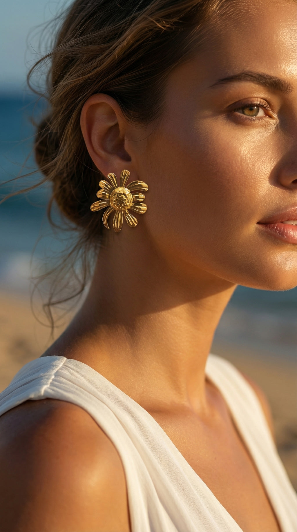 Woman wearing gold sunflower earrings with a blurred beach background
