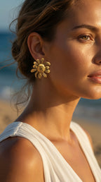 Woman wearing gold sunflower earrings with a blurred beach background
