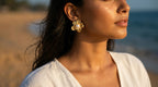 Woman wearing gold earrings with a blurred beach background