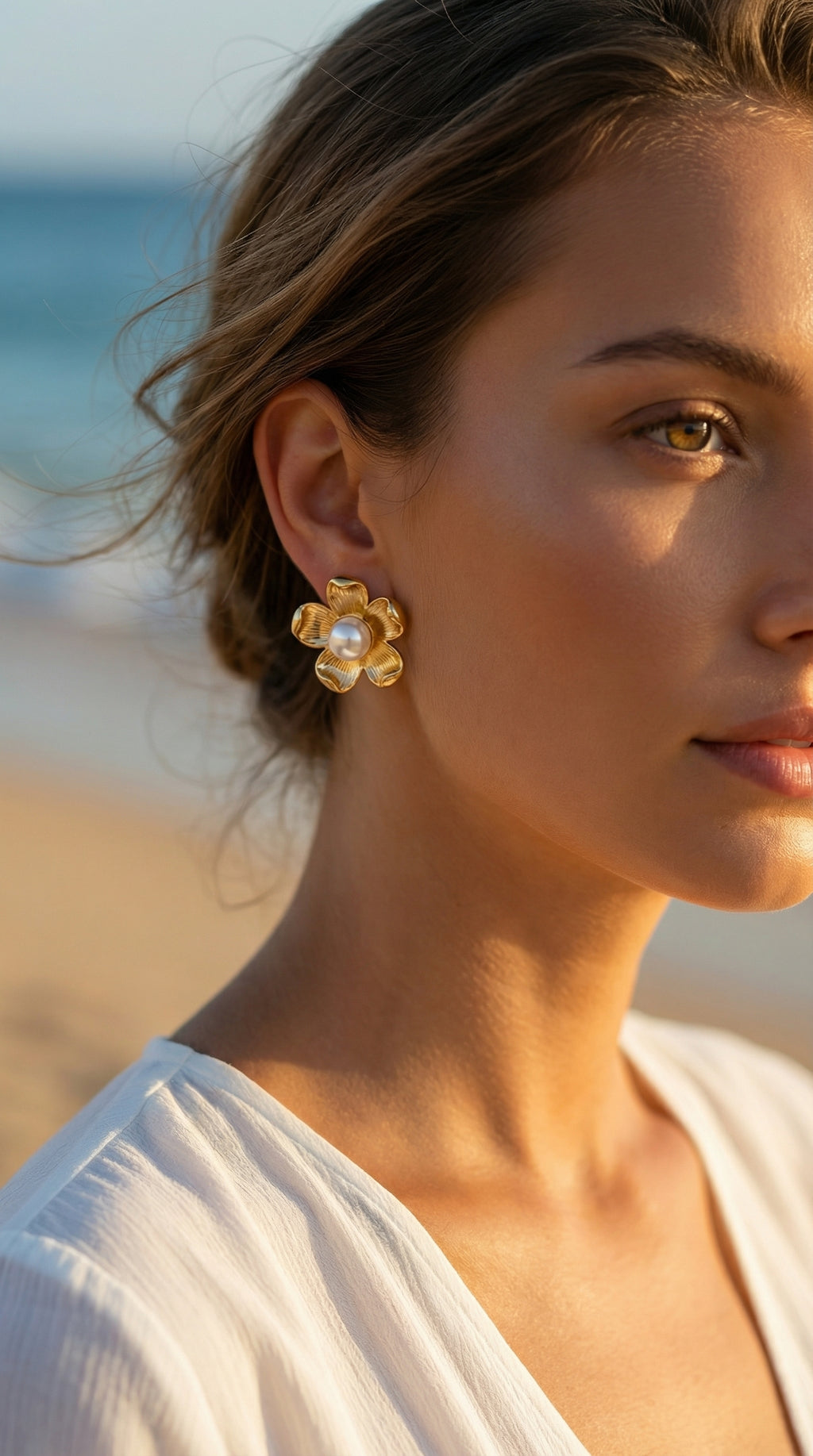 Woman wearing gold earrings with pearls on a beach