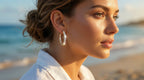 Woman wearing hoop earrings on a beach with ocean in the background