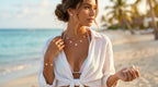 Woman on a beach wearing a white outfit with jewelry, with ocean and palm trees in the background.