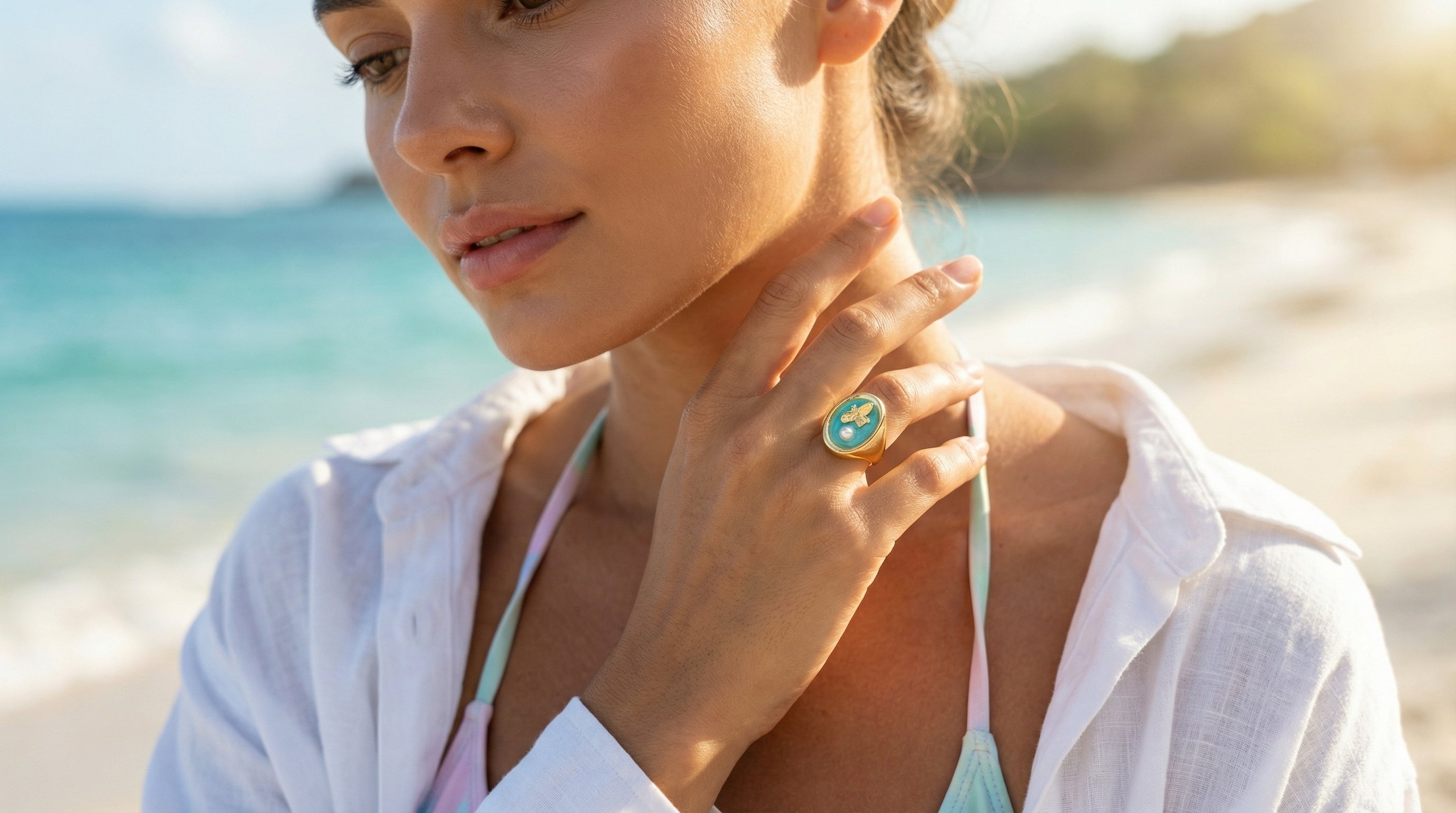 Woman on a beach wearing a white shirt and green ring with a blue gemstone.