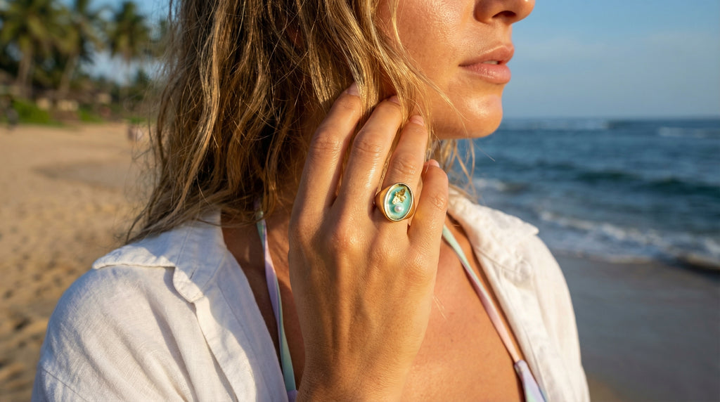 Woman on a beach wearing a white shirt and a ring with a green gemstone.