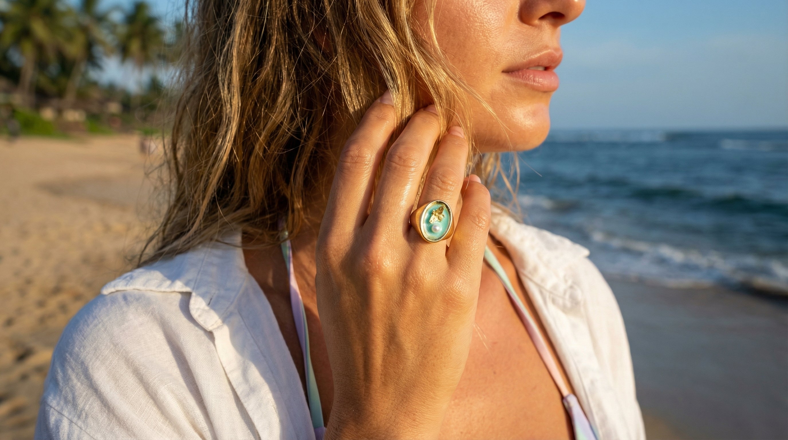 Woman on a beach wearing a white shirt and a ring with a green gemstone.
