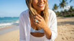 Woman on a beach wearing a white outfit with a ring, surrounded by ocean and palm trees.