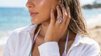 Woman on a beach wearing a white shirt and a ring with a purple gemstone.