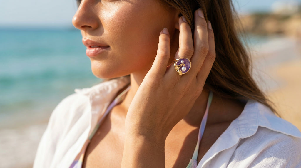 Woman on a beach wearing a white shirt and purple ring with a blue stone.