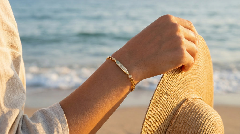 Person wearing a gold bracelet on a beach with ocean in the background