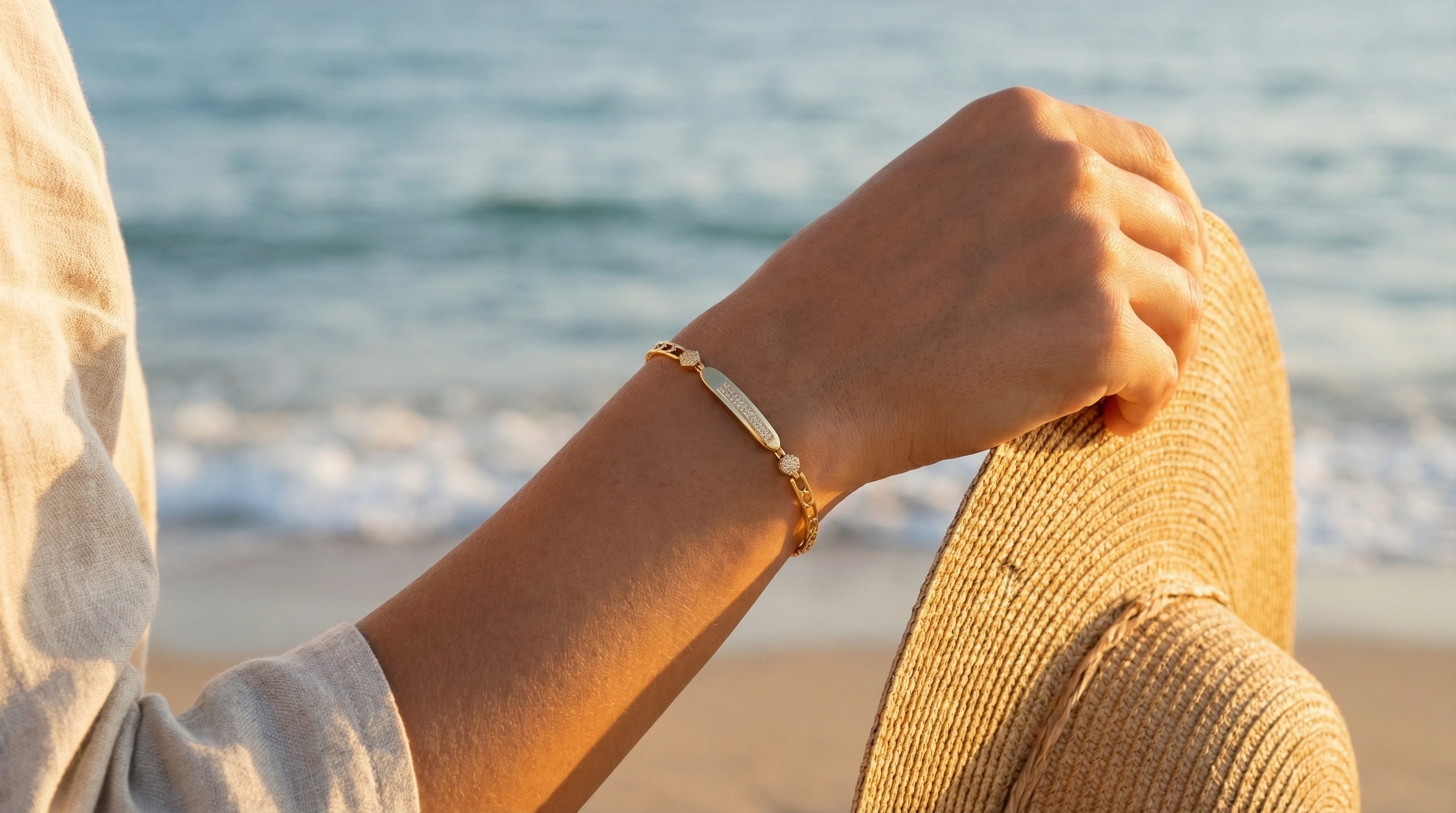 Person wearing a gold bracelet on a beach with ocean in the background