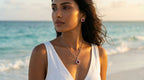 Woman on a beach wearing a white sleeveless top and red earrings with a necklace.