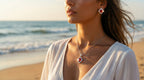 Woman on a beach wearing earrings and a necklace with a blurred ocean background