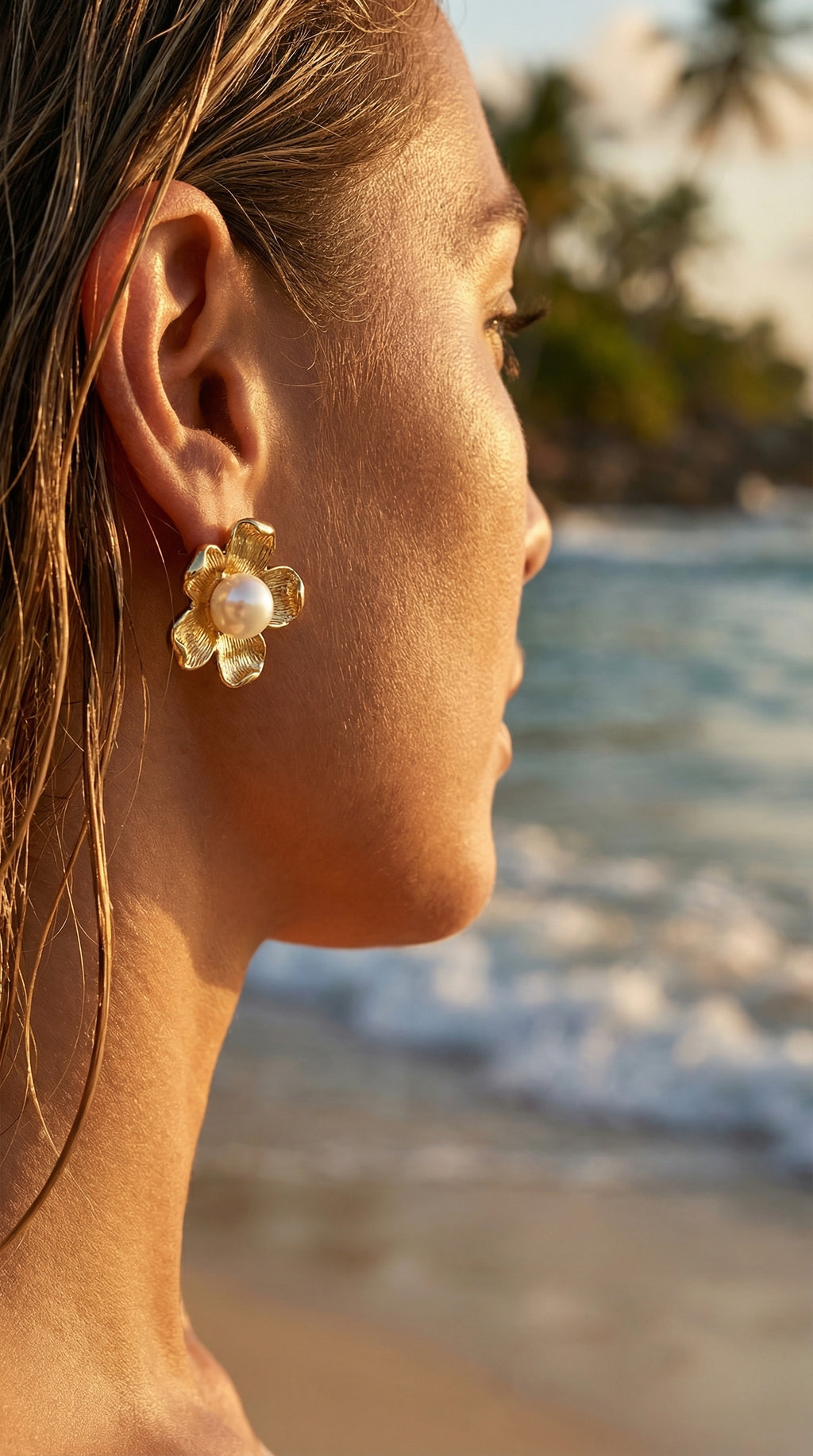 Woman wearing gold floral earrings with a blurred beach background