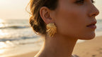 Woman wearing gold earrings with a beach background