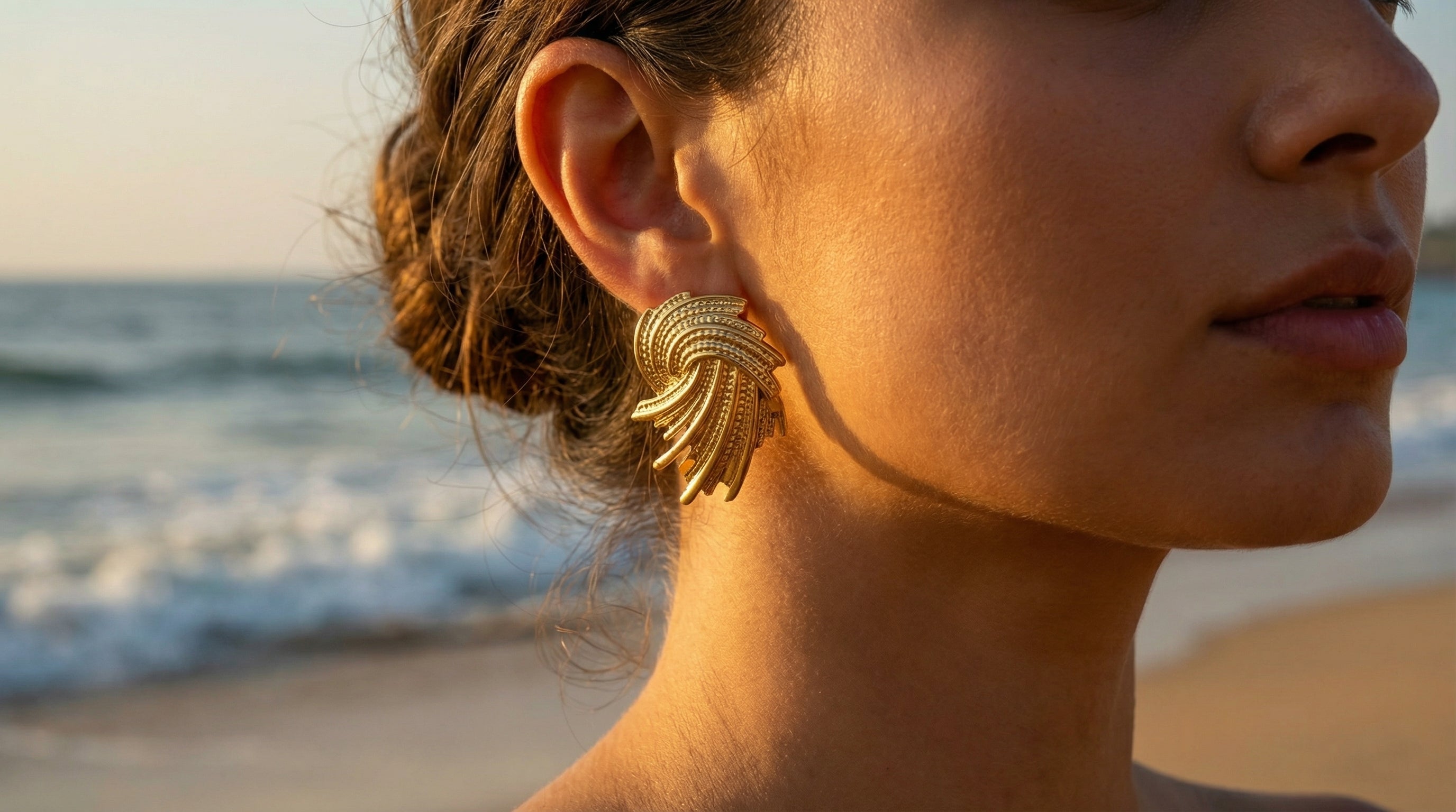 Woman wearing gold earrings with a beach background