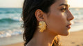 Woman wearing gold earrings on a beach with ocean in the background