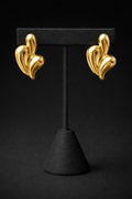Gold earrings on a black stand against a black background