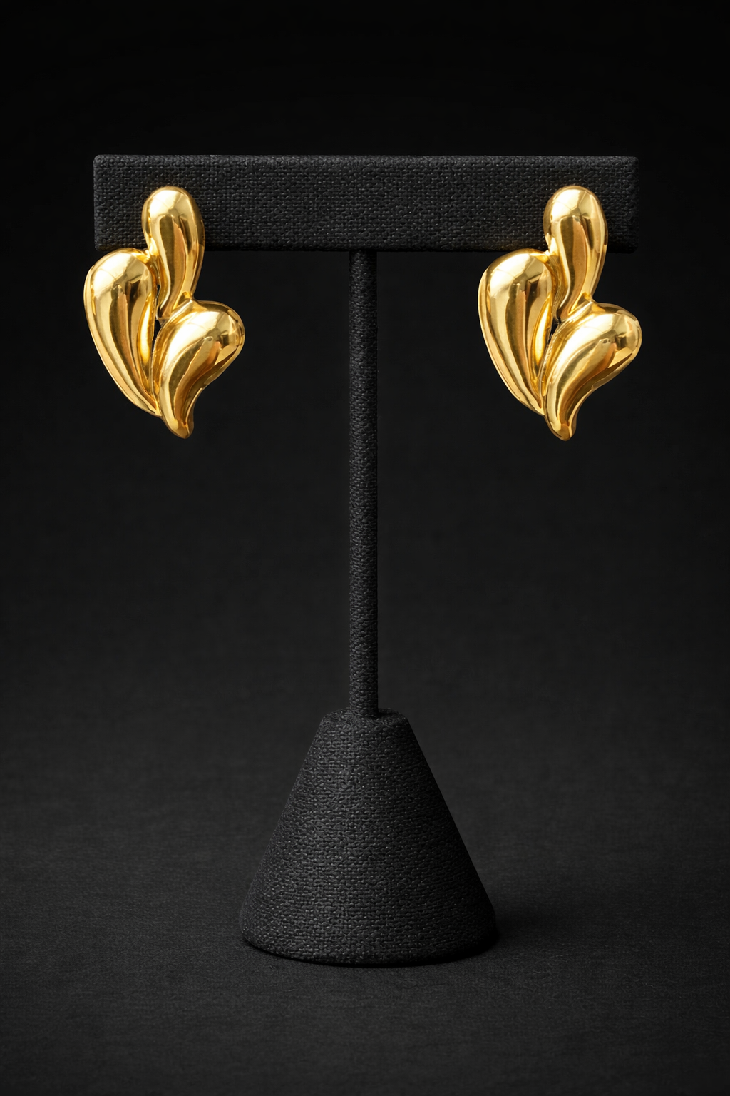 Gold earrings on a black stand against a black background