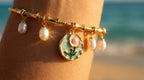 Gold bracelet with charms on a person's wrist against a beach background