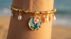Gold bracelet with floral charm and pearls on a blurred beach background