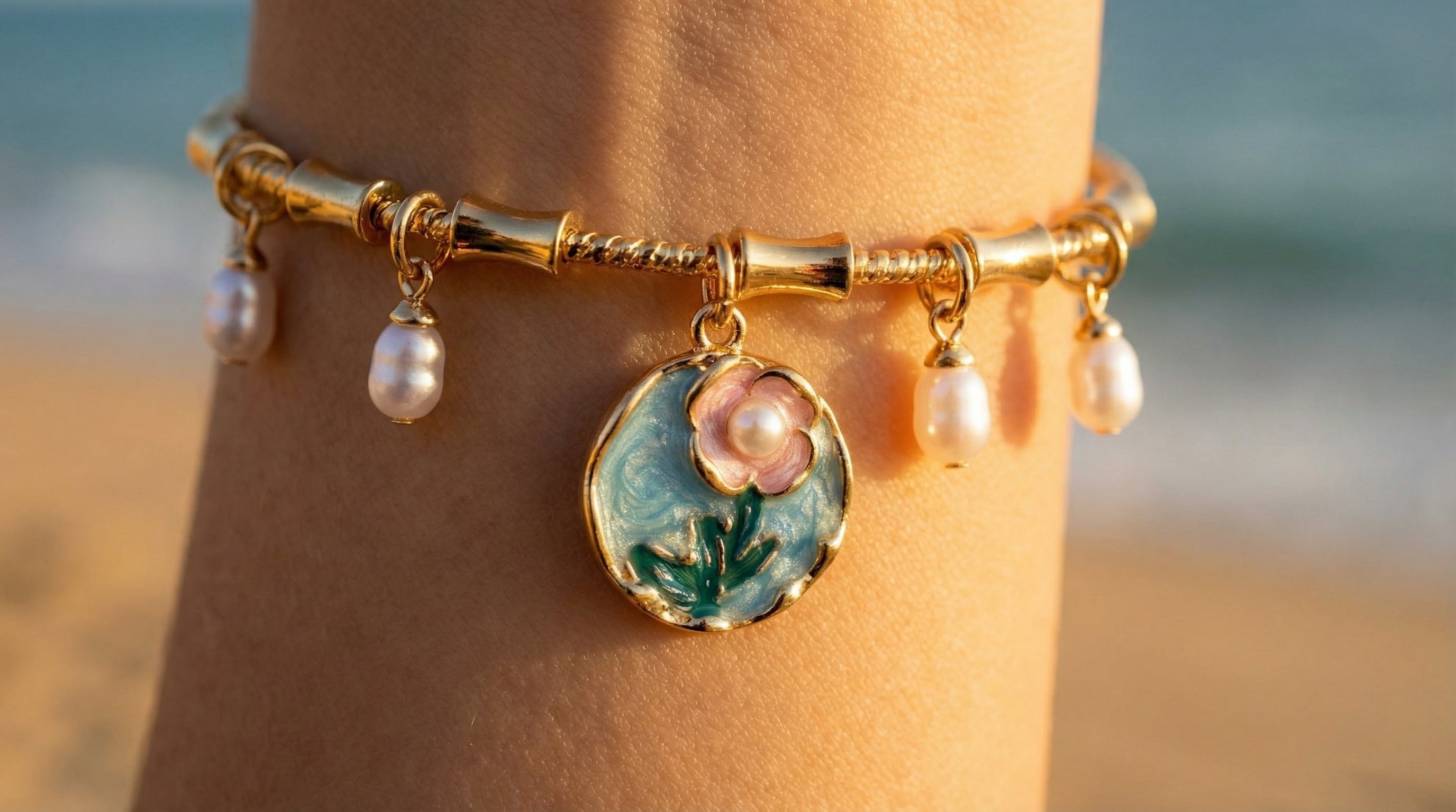 Gold bracelet with floral charm and pearls on a blurred beach background