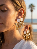 Close-up of a woman wearing gold earrings with a blurred beach background