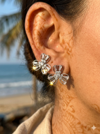 Close-up of a person wearing silver flower earrings with a beach background