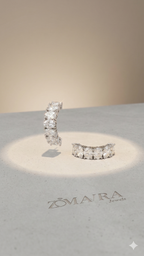 Pair of diamond earrings on a branded stand with Zomra Jewels logo.