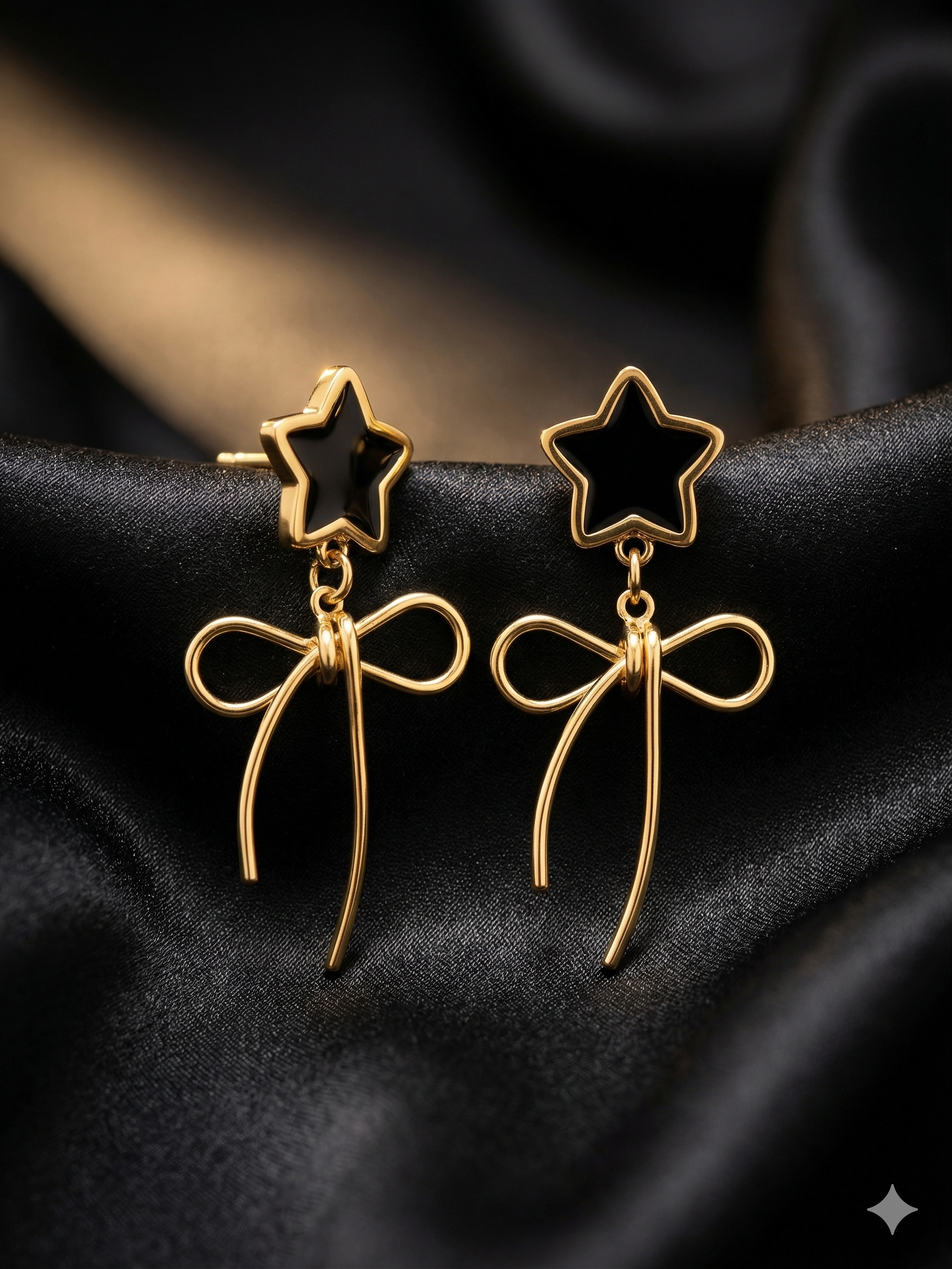 Gold star and bow earrings on a black fabric background