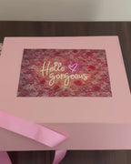 Gift box with various items including a teddy bear, snacks, and beauty products on a dark surface.
