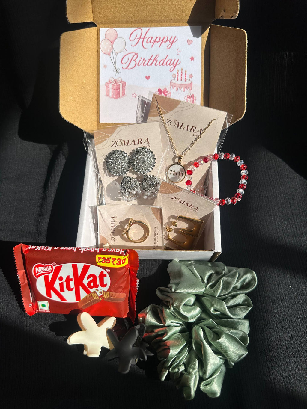 Gift box with jewelry, a scrunchie, and KitKat candy on a dark surface.