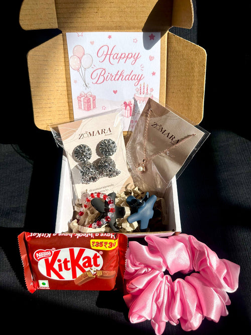 Gift box with birthday card, earrings, and a pink scrunchie on a dark surface
