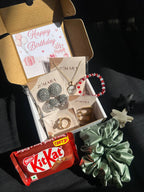Gift box with jewelry, a scrunchie, and a KitKat bar on a dark surface.