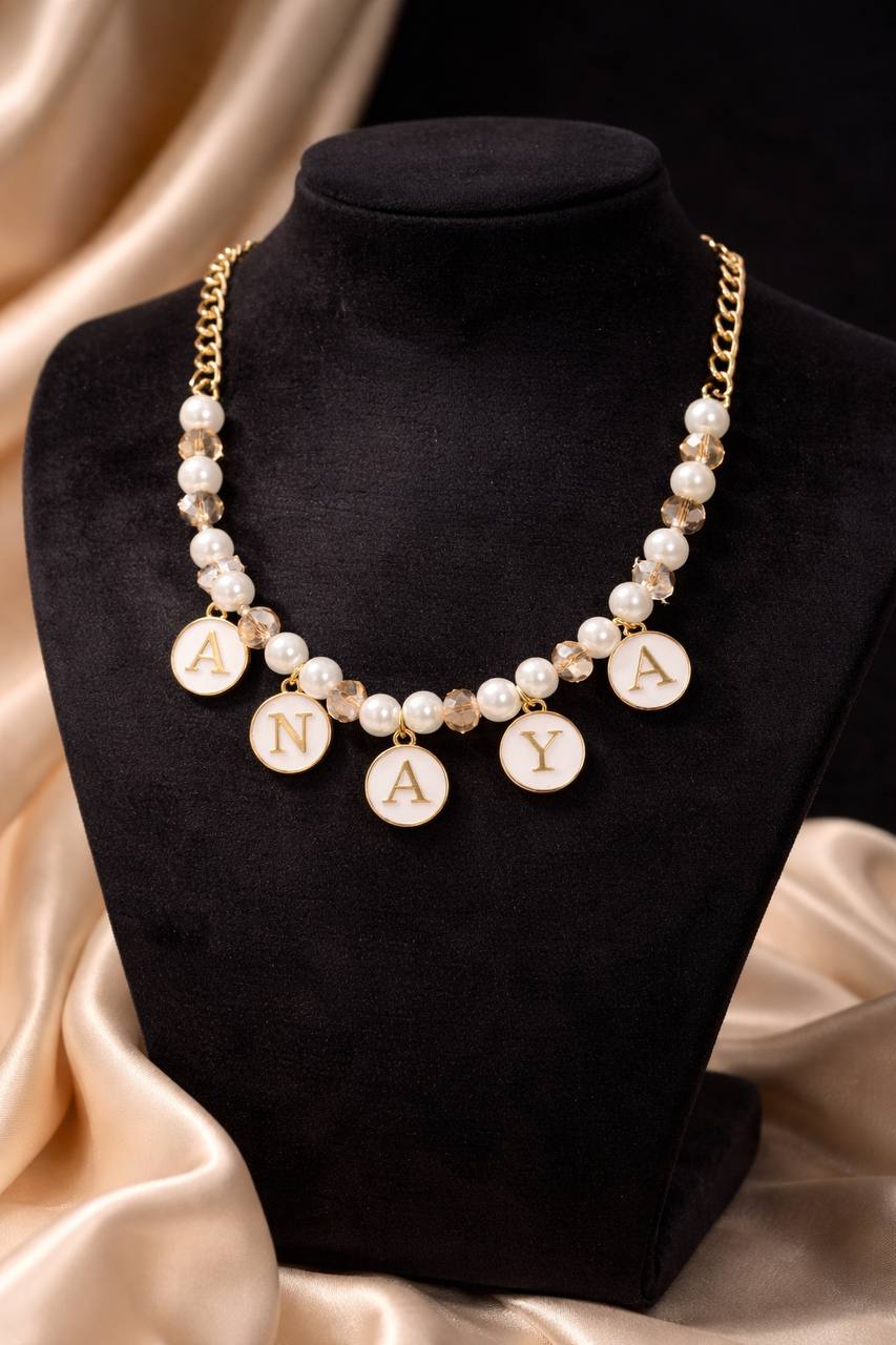 Pearl necklace with 'ANAYA' charms on a black stand with beige fabric background