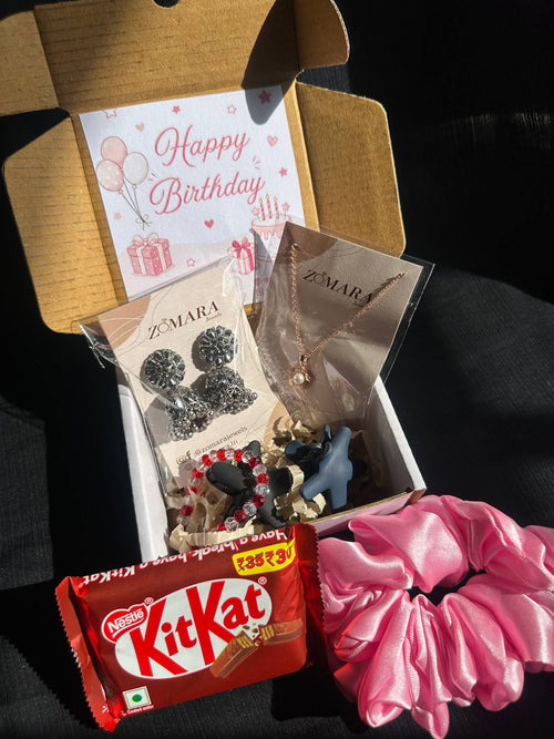 Gift box with jewelry, a pink scrunchie, and KitKat chocolate on a dark surface.