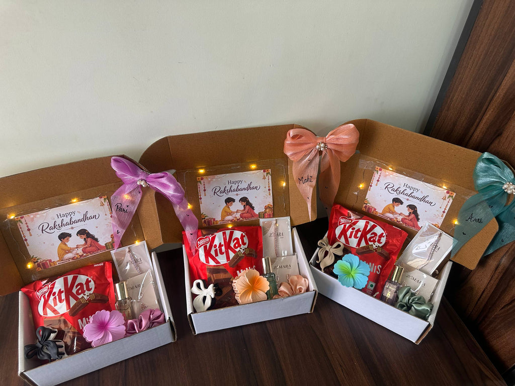 Three open gift boxes arranged on a dark wooden surface, each containing a red KitKat, a small card, decorative flowers, and ribbon bows. The boxes are photographed indoors against a plain light wall.