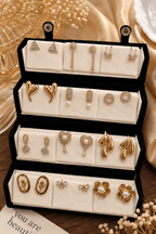 "12-pair gold-tone earring set featuring crystal triangle studs, pearl drops, floral earrings, bow studs, heart earrings, and statement fashion designs displayed on a jewelry stand."